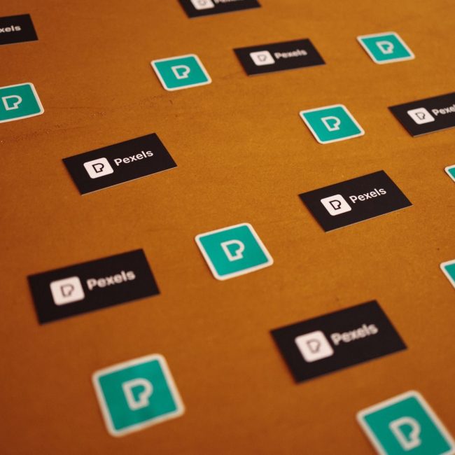 Pexels logos and stickers scattered on a brown background in a creative pattern.