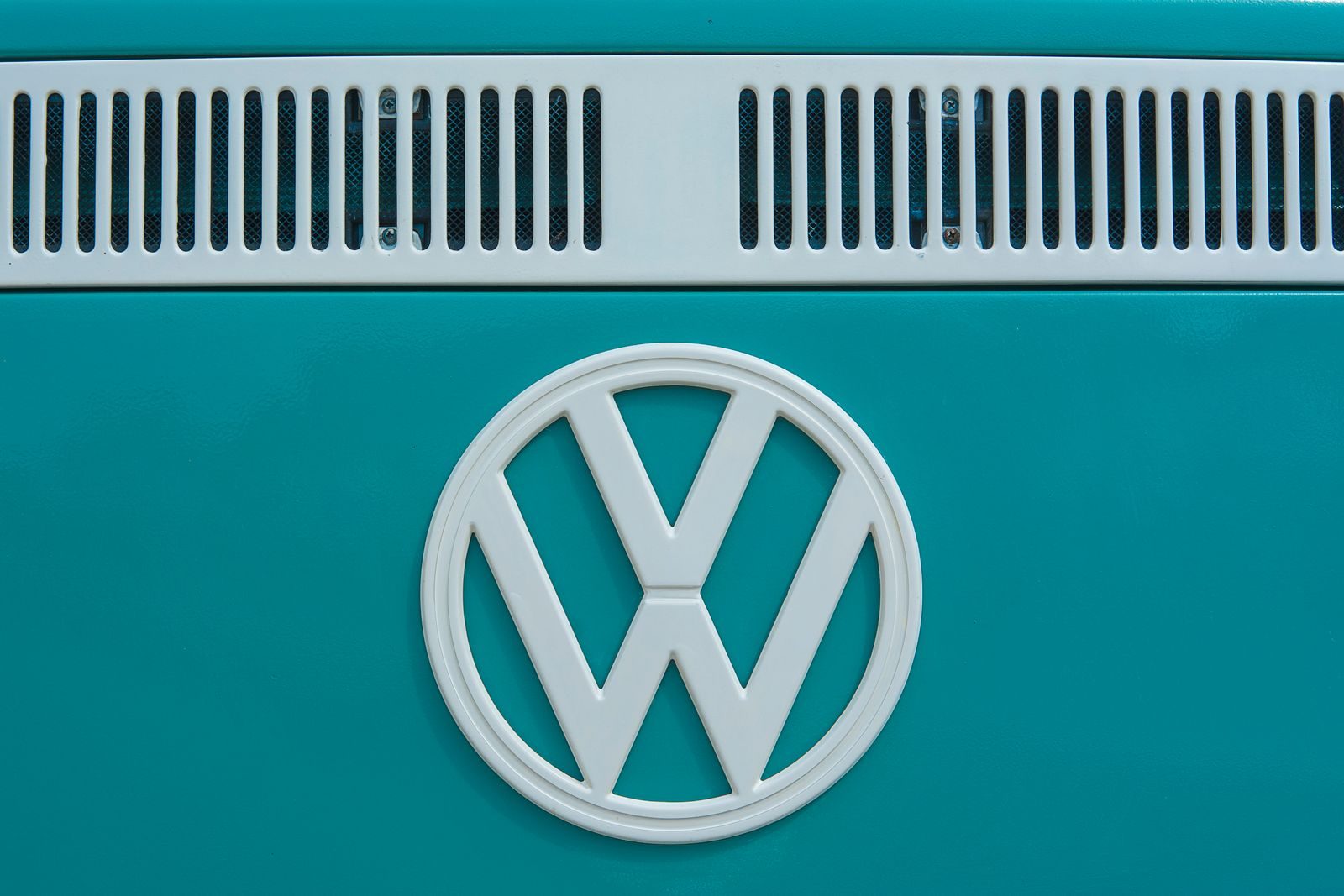 Close-up of a vintage Volkswagen emblem on a teal van, showcasing classic design and color.