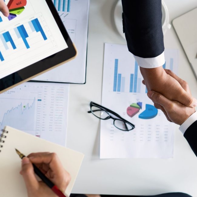 Business professionals handshake over graphs and charts in a corporate setting, symbolizing successful negotiation and agreement.