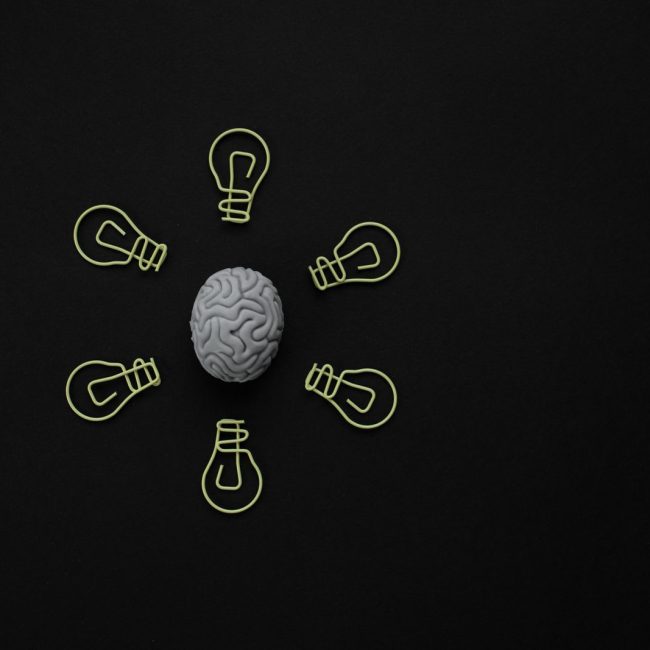Conceptual photo of a brain surrounded by light bulb clips on black background.