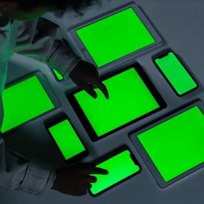 A variety of electronic gadgets with green screens being interacted with indoors.