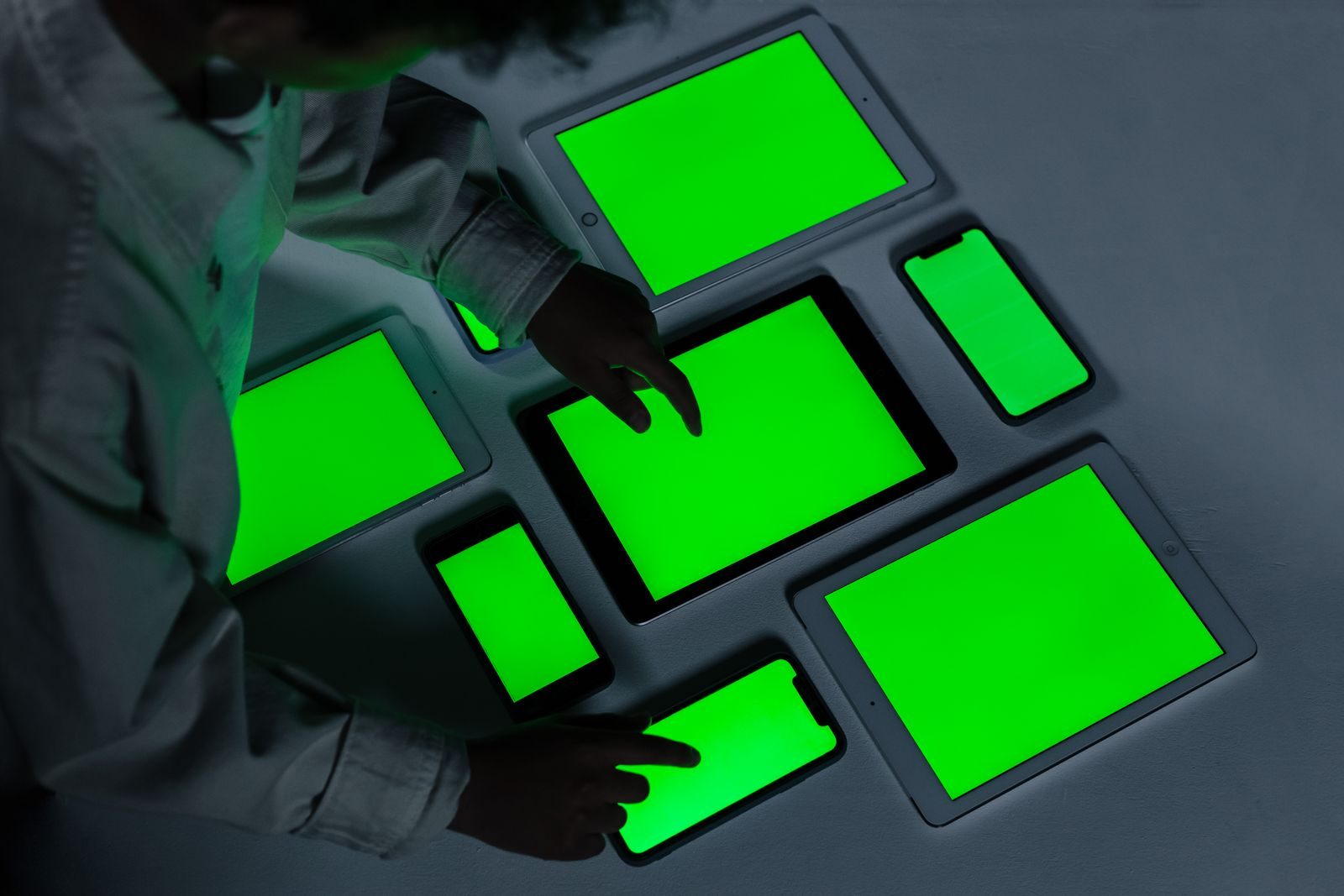 A variety of electronic gadgets with green screens being interacted with indoors.