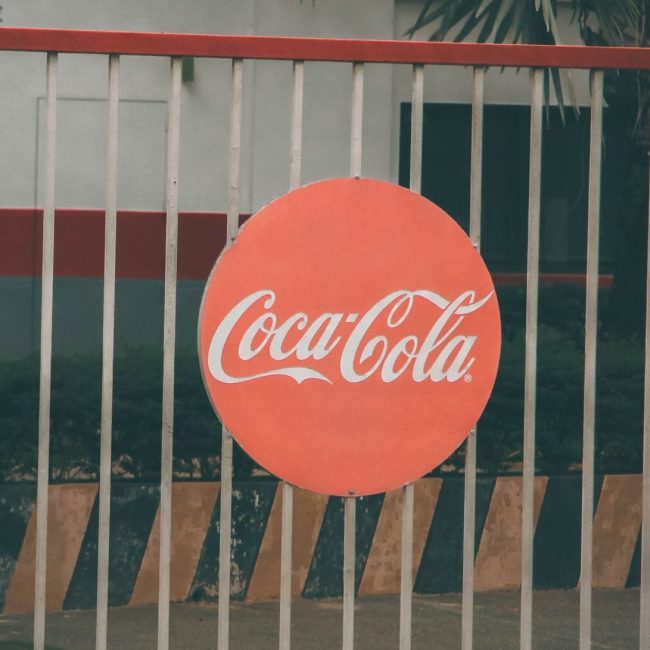 Coca-Cola logo prominently displayed on outdoor fence, urban setting.