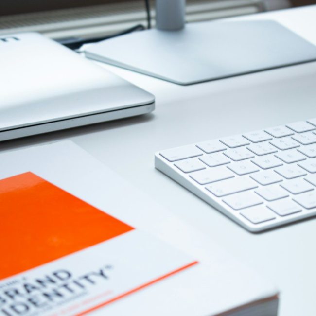 A white keyboard, laptop, and book on a clean desk in a workspace
