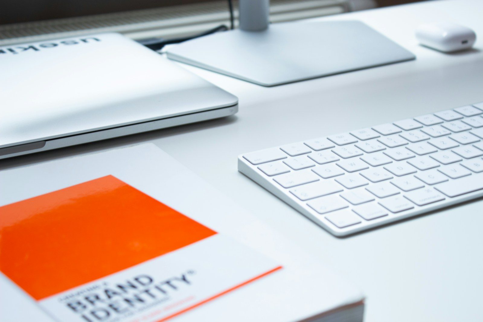A white keyboard, laptop, and book on a clean desk in a workspace