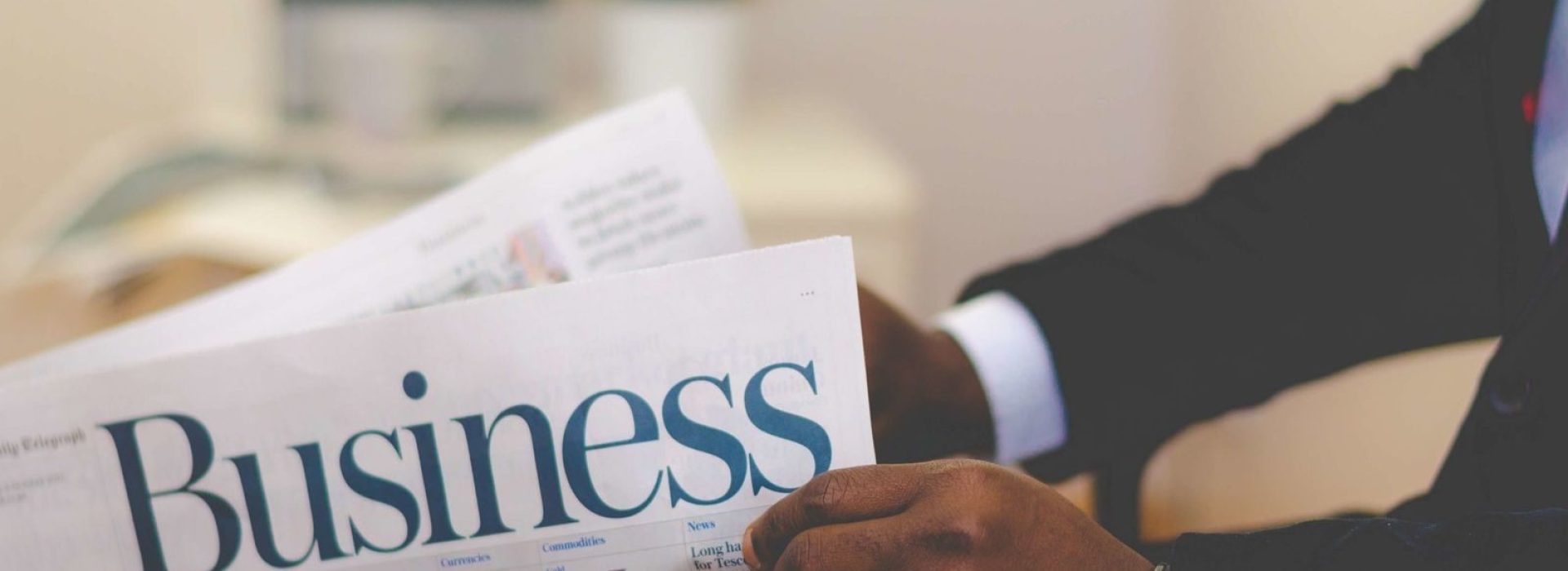 Close-up of a businessman reading a newspaper indoors, focusing on business headlines.
